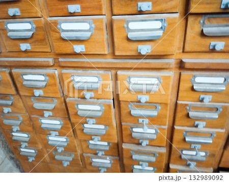 Vintage wooden drawer cabinet with metal handles and label holders, open empty drawer in old library card catalog filing system, retro office furniture storage unit with rustic archive organization 132989092
