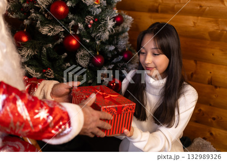 Santa gives the girl a Christmas gift in a red gift box. Santa gives the girl a Christmas gift in a red gift box. 132989326