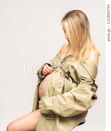 28 week, Elegant maternity portrait of pregnant woman in beige trench coat. Natural makeup and minimal studio light emphasize femininity and calm mood 132994750