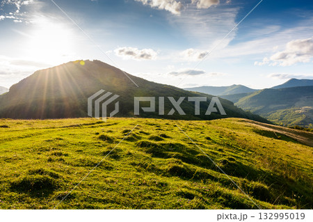 beautiful countryside at sunset. wonderful summertime landscape in mountains in evening light. scenic view of grassy field and rolling hills. rural scenery storytelling image under the rainbow 132995019