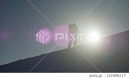 Determined mountaineer ascending snowy slope against sunlight 132996217