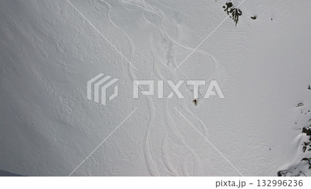 Skier leaving tracks on pristine snow field near rocky cliffs Skier leaving tracks on pristine snow field near rocky cliffs 132996236