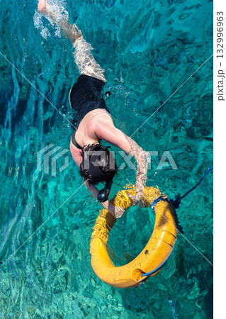 A woman looks at the underwater world with her head in the water and holding onto a lifebuoy A woman looks at the underwater world with her head in the water and holding onto a lifebuoy 132996963
