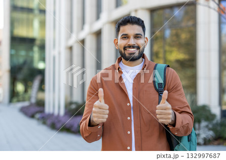 Confident young man wearing casual clothes standing outdoors, giving thumbs up with a bright smile. This positive gesture emphasizes assurance, happiness, and encouragement. Ideal for themes centered 132997687