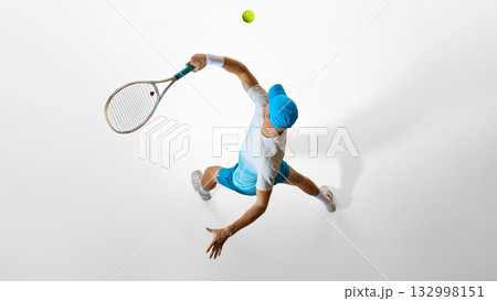 Tennis player in bright blue uniform preparing serve captured from above on white studio floor 132998151