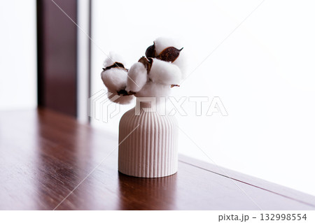 A white ceramic vase with a ribbed texture holds cotton branches. The background is bright and minimalistic, emphasizing the simplicity of the decor A white ceramic vase with a ribbed texture holds cotton branches. The background is bright and minimalistic, emphasizing the simplicity of the decor 132998554