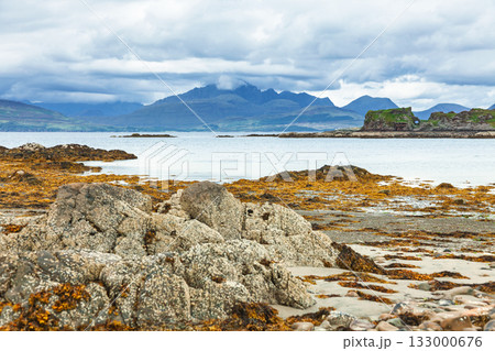 Dunscaith Castle ruins and Cuillin mountains seen across rocky shore Isle of Skye Scotland 133000676