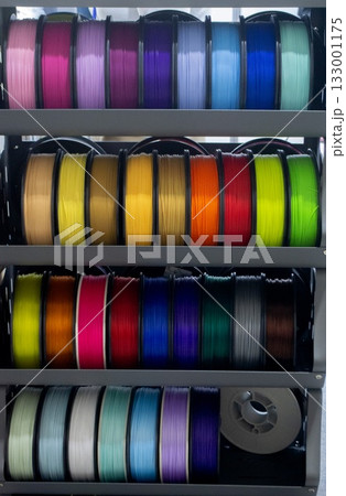 Many spools with multi-colored plastic for 3D printing. Spools with pink, red, burgundy, purple, yellow, orange blue plastic wire for 3D printer. Components for 3D printing. Accessories for 3D printer 133001175