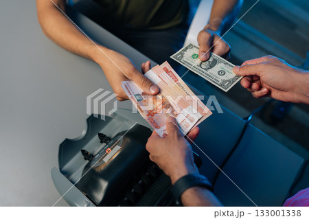 Close-up cropped shot of unrecognizable bank employees or cashiers exchanging Russian rubles and us dollars at exchange office, using money counting machine to ensure accuracy in transaction. 133001338