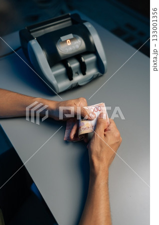 Close-up top view of cashier counting Russian rubles banknotes late at night after closing store using money counting machine in background. Concept of financial accounting in modern office. 133001356
