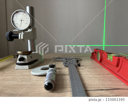 Photograph of a caliper, a measuring tape, and a level on a wooden surface. Measuring instruments in metrology. Photograph of a caliper, a measuring tape, and a level on a wooden surface. Measuring instruments in metrology. 133001395