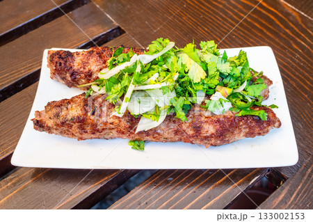 Georgian meat kebab on white plate on wooden table 133002153