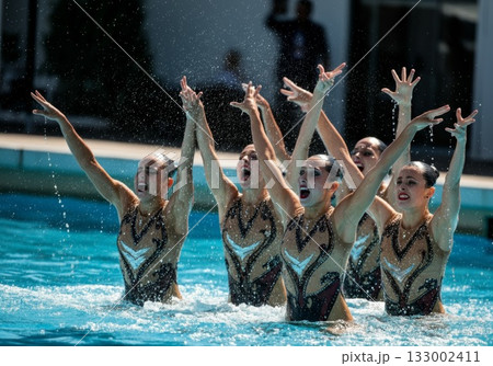 Synchronized swimmers performing a dynamic routine in a bright blue pool with splashes of water 133002411