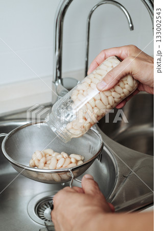a man pouring white beans into a sieve a man pouring white beans into a sieve 133002543