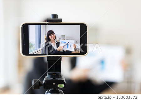 Caucasian woman presenting business charts and growth analysis while being recorded through smartphone setup Caucasian woman presenting business charts and growth analysis while being recorded through smartphone setup 133003572
