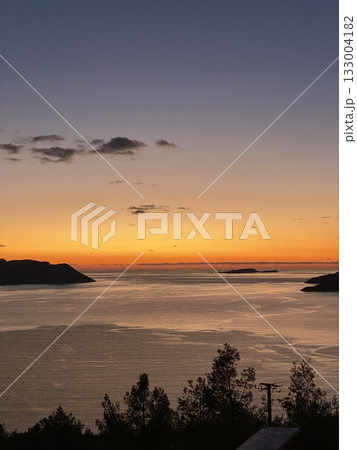 Sunset sky over serene ocean with distant islands, reflected on water, creating a tranquil background 133004182