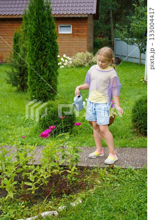 Happy young girl taking care of her garden, watering flowers with a watering can on a sunny summer day, enjoying outdoor activity and gardening Happy young girl taking care of her garden, watering flowers with a watering can on a sunny summer day, enjoying outdoor activity and gardening 133004417