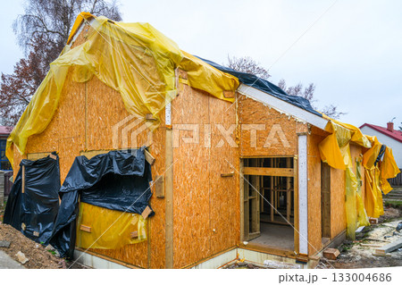 Wooden house under construction covered with plastic sheets for weather protection in autumn 133004686