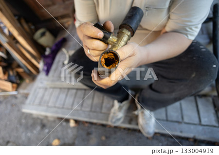A cross-section of an old clogged water pipe A man holds a section of an old metal water pipe, examining a thick layer of rust and mineral deposits indicating severe corrosion in the plumbing system. 133004919