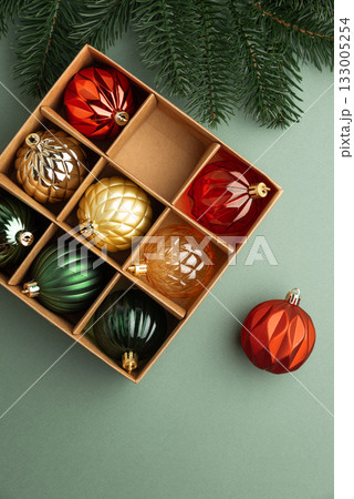 Box of Christmas Ornaments in Festive Colors with Fir Tree Branch on Green Background Box of Christmas Ornaments in Festive Colors with Fir Tree Branch on Green Background 133005254