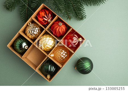 Box of Christmas Ornaments in Festive Colors with Fir Tree Branch on Green Background Box of Christmas Ornaments in Festive Colors with Fir Tree Branch on Green Background 133005255