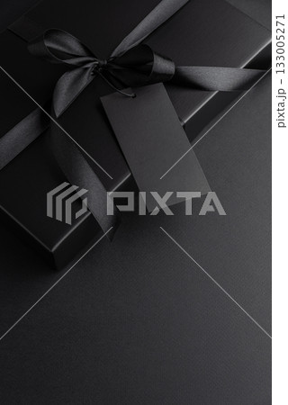 Black Gift Box with Satin Ribbon and Blank Tag on Dark Background Black Gift Box with Satin Ribbon and Blank Tag on Dark Background 133005271