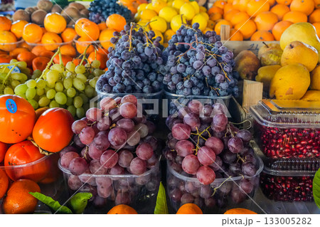 Assorted grapes of different colors with citrus fruits and persimmons displayed at a market stand. Ideal for food backgrounds, grocery, and healthy eating visuals. 133005282