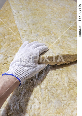 a gloved hand takes a sheet of thermal insulation material 133005410