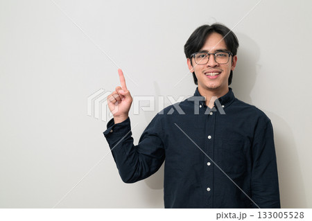 Young Asian businessman wearing eyeglasses pointing and showing copy space against white background 133005528