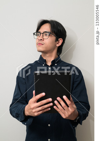 Portrait of young Asian Thai man wearing eyeglasses using digital tablet computer and thinking 133005546
