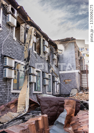 Ground level view of fire damaged building blackened brick walls broken windows twisted metal debris and intact AC units contrast with collapsed roof and scorched upper facade. Ground level view of fire damaged building blackened brick walls broken windows twisted metal debris and intact AC units contrast with collapsed roof and scorched upper facade. 133006275
