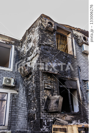 Ground level view of fire ravaged brick building blackened walls, melted AC units, shattered windows, and exposed interior reveal extensive heat damage and structural vulnerability. Ground level view of fire ravaged brick building blackened walls, melted AC units, shattered windows, and exposed interior reveal extensive heat damage and structural vulnerability. 133006276