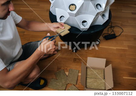 High-angle view of gardener male cutting rockwool with scissors, preparing hydroponic media for seed starting, highlighting precision in indoor cultivation techniques. Concept of home gardening. 133007112