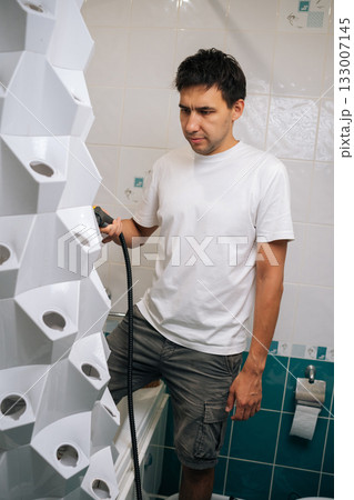 Vertical portrait of gardener sanitizing vertical hydroponic tower garden with steam cleaner in bathroom, highlighting innovative indoor gardening and cleaning technique. Concept of home gardening. 133007145