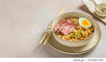 Ramen or asian style noodles soup with beef, egg and green onions in bowl on light beige background, space for text Ramen or asian style noodles soup with beef, egg and green onions in bowl on light beige background, space for text 133007169