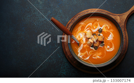 Pumpkin soup croutons cream fresh pumpkin slices wooden board dark background autumn winter copy space 133007174