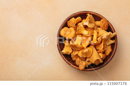 Fresh chanterelle mushrooms in a a rustic bowl on warm beige background top view, space for text 133007178