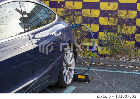 A modern electric car is charging at an electric charging station. A modern electric car is charging at an electric charging station. 133007332