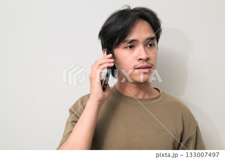 Portrait of handsome young Asian Thai man talking on the phone against white background Portrait of handsome young Asian Thai man talking on the phone against white background 133007497