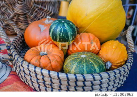 Horizontal shot of pumpkins neatly arranged in a basket on a table, complemented by potted chrysanthemums and seasonal colors. Ideal for fall, harvest, market, lifestyle, and background use. 133008962