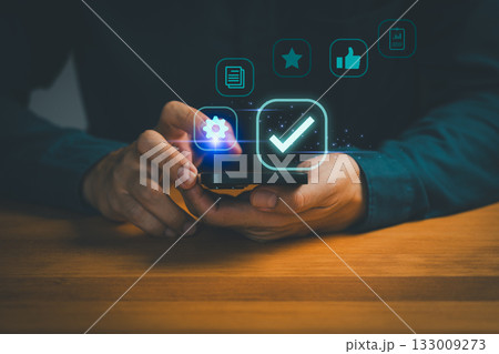 Person holding smartphone with digital icons of settings, checkmark, star, like, and documents, symbolizing mobile app approval, user satisfaction, quality assurance and digital technology management. Person holding smartphone with digital icons of settings, checkmark, star, like, and documents, symbolizing mobile app approval, user satisfaction, quality assurance and digital technology management. 133009273