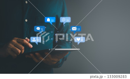 Man using digital tablet with floating social media notification icons, symbolizing online communication, messaging, email, followers, likes, and digital network connectivity. 133009283