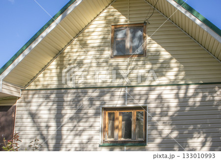 House facade with beige siding and wooden windows sunny shadows 133010993