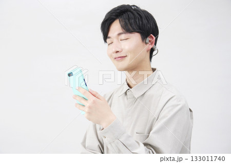 骨伝導イヤホンをつけて音楽を聴く20代男性 白背景 骨伝導イヤホンをつけて音楽を聴く20代男性 白背景 133011740