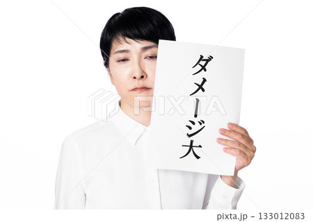 ダメージ大と書かれた紙を持ち疲れた様子の白いシャツを着たシニア女性 ダメージ大と書かれた紙を持ち疲れた様子の白いシャツを着たシニア女性 133012083