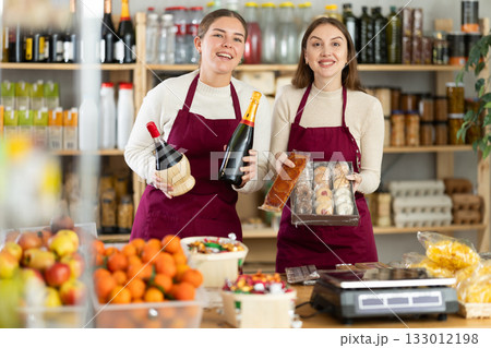 Young saleswomen are holding champagne, wine and sweets in their hands. 133012198