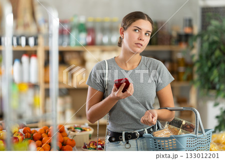 Young woman with phone choosing groceries in store Young woman with phone choosing groceries in store 133012201