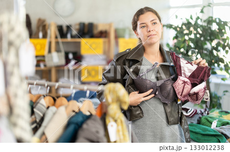 Young woman choosing underwear and bras in clothing store near hangers Young woman choosing underwear and bras in clothing store near hangers 133012238