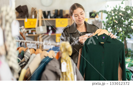 Young woman choosing a warm wool dress on sale in a store 133012372