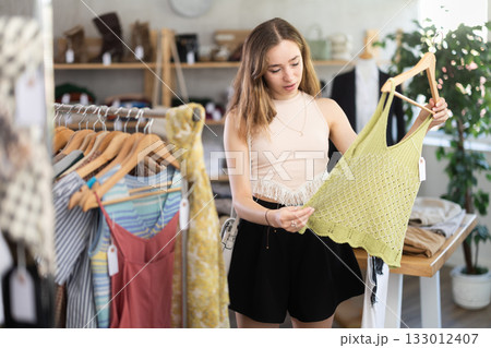 Selective young woman choosing something for summer in clothing store 133012407